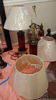 Two red glass cylinder lamps with thick brass-colored plastic bases, surrounded by three neutral canvas lampshades wrapped in plastic.