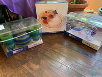 Three boxed JCPenney Home serving ware sets including a blue and green 25 piece party set, a striped 6 piece margarita glass set, and a striped 2 piece chip and dip set.