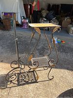 Photo showing metal plant stand with wicker top, gold-painted leaves, and metal candle stand in outdoor lighting with some items and people in background.