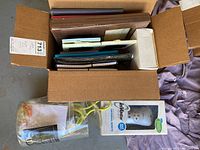 Open box showing tablet cases, notebooks, photo album, CD case, and picture frames stacked inside