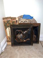 Five wall art pieces stacked, showing two metal teapot plaques in wooden frames in front and three taller decorative plaques behind with palm tree and wine bottle designs.