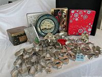 Wide view of multiple metal cookie cutters, three decorative cookie tins, and the black baking tray behind.
