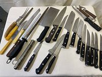 Full set of assorted kitchen knives along with sharpeners and fork laid out on white surface