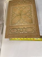 Close-up of carved wooden box lid showing detailed geometric carving and bead inlay, with a measuring tape showing width approx 23 cm