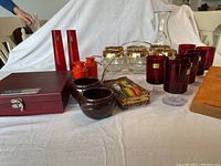 Photo showing full lot view including red glasses, crystal dish with gold bowls, red wooden box, ceramic and orange condiment containers, glass carafe, and wooden cutting board.
