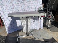 Front view of ironing board with iron attached and laundry hamper underneath