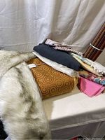 Photo showing various folded textile fabrics including white faux fur, mustard upholstery fabric with circular pattern, grey textile, and other mixed fabric pieces.
