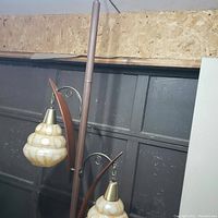 Full view of the tension pole lamp showing wood-tone pole and two hanging glass shades with amber patterns, near a wall and table.