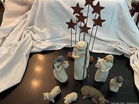 Overall view of the nativity scene figurines with star decorations showing scale and condition on a black surface with a white cloth background.