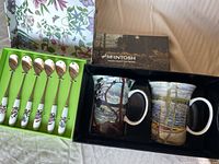 Box containing two McIntosh ceramic mugs with Tom Thomson artwork and a boxed set of six floral Portmeiron teaspoons.