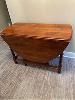 Closed view of the antique oak gate leg table showing medium brown oval top and barley twist legs folded in.