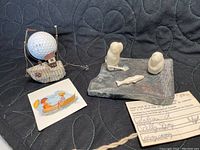 Overall lot showing Inuit soapstone carving, quonset fishing boat model, golf ball for size comparison, and certificate of authenticity for carving