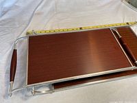 Top view of one serving tray showing the wood grain Formica surface, metal frame, and wooden handles. A measuring tape for scale indicates approximately 21 inches in length.