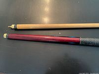 Pool cue pieces shown with focus on ends that unscrew at midpoint, displaying natural wood shaft and reddish handle with worn black grip