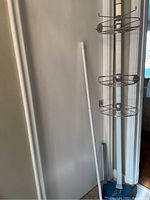 Photo of the Simplehuman corner shower caddy installed in a corner, showing the four circular metal baskets and the white adjustable rod next to it.