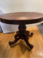 Full view of antique finish hardwood round tilt top table with pedestal base and four curved legs.