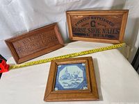 Three framed pieces: two wooden framed vintage box labels and one wooden framed blue and white ceramic tile.