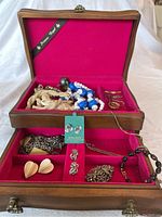 Open wood jewelry box showing all assorted jewelry items on red velvet lining inside the box with multiple compartments.