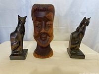 Front view of wooden head sculpture flanked by two metal cat bookends
