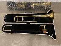 Full view of Holton trombone in open case showing brass instrument, mouthpiece, valve oil, and black fabric lining inside case.