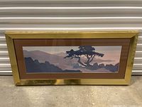 Full frontal image of the large framed landscape art piece with brown mat and gold-tone frame on concrete floor.