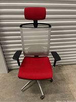 Front view of office chair showing red cushioned seat and headrest, white mesh backrest, black armrests, and aluminum base with casters