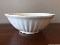 Side view of large white ceramic mixing bowl showing fluted design and wear on rim
