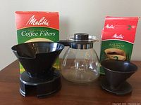 Photo of the Melitta glass coffee carafe with black plastic #6 and #2 drip baskets and partial boxes of Melitta coffee filters