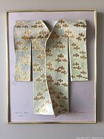 Front view of the framed raku porcelain kimono art by Diana Friedman showing three-dimensional form, gold metal frame, and taupe mat.