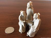 Small pottery figurine of three men playing Go, placed next to a quarter for scale.