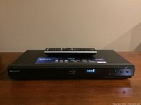 Front view of Sony BDP-S350 Blu-ray player powered on with front display showing 'HOME' and remote control placed on top.