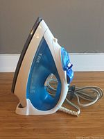 Side profile of T-fal Ultraglide Diffusion steam iron showing white and blue body with attached electrical cord and water reservoir.