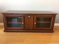 Front view of wood TV stand with two glass doors and center wooden door closed.