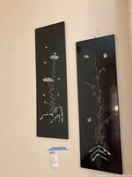 Front view of two mounted black lacquered panels side by side showing mother of pearl inlay with flowers, bamboo, birds, and mountain motifs.