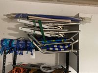 Shelved view of folded beach chairs with metal frames and blue fabric, blue folded beach umbrella, and blue rolled blanket.