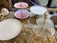 Full set of cake plates and sandwich servers including two tiered stands and single cake plates shown on granite countertop.