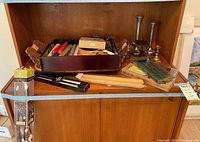 Overview of the arrangement showing wooden trays filled with assorted candles, some unboxed and some in packages, plus candle holders and a boxed wine accessory set on top of a wooden cabinet.