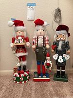 Three Christmas nutcracker figures standing side by side against a wall, showing full height and details.