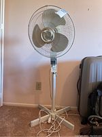 Full view of the white floor standing fan showing mesh guard, blades, adjustable pole, and cross base.