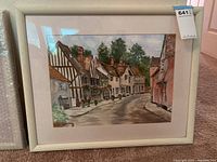 Full view of the framed watercolor painting showing the village street with Tudor style buildings and flower boxes.