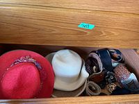 Photo showing red floral hat, white woven hat, and multiple belts in wooden drawer
