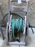 Front view of the light green garden hose wound on the portable plastic hose reel caddy with handle and wheels.