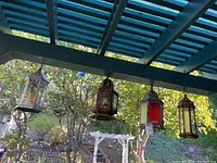 Four different outdoor hanging lanterns viewed from below under a blue pergola, showing metal frames and colored glass panels