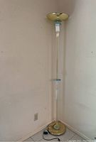Full view of the lucite and metal floor lamp standing in a corner, showing its tall clear lucite column and brass/gold-tone metal base and canopy.