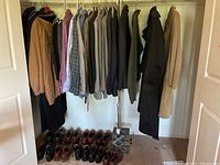 Photo showing men's clothing hanging on a rack including shirts, jackets, and outerwear with men's shoes arranged underneath.