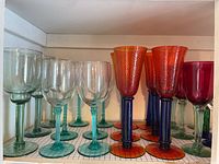 Mixed colored and clear wine glasses arranged on shelf, showing variations in stem and glass colors