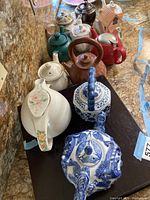 View of the entire collection of approximately 11 teapots and one tea caddie arranged on a counter.