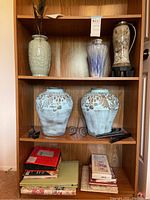 Shelving unit with six decorative vases of various sizes and colors, and some photo albums and frames on lower shelves.