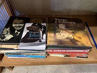 View of vinyl records stacked on a shelf including "Tango y Folklore" and a book titled "Converismos de Tango" among others.