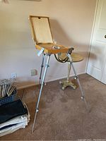 Wooden collapsible art easel standing upright with tripod legs extended, showing the closed storage box and hinged canvas support panel.
